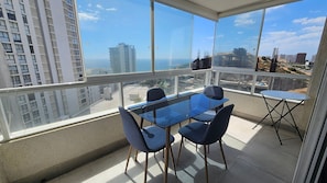 A balcony with a glass table and chairs, a small folding table, and a view of the cityscape and buildings. - Oceana Suites Reñaca Norte (Vina del Mar)