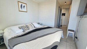 Un dormitorio con una cama, una mesita de noche, un cuadro enmarcado en la pared y una puerta que da a otra habitación.
