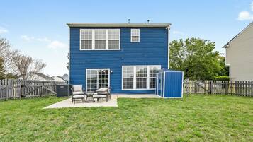 Une maison bleue à deux étages, dotée d’un patio, d’une clôture en bois et d’une antenne parabolique.