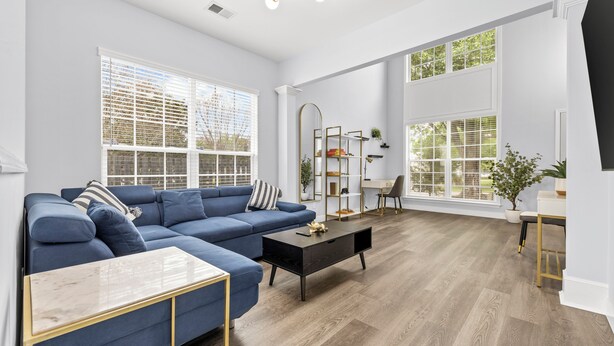 Un salon spacieux avec un canapé d’angle bleu, une table basse en verre et un plancher en bois.