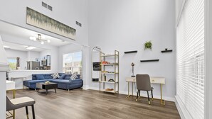 Un salon moderne avec un canapé bleu, un bureau et une chaise. On y trouve une bibliothèque et une plante accrochée au mur.