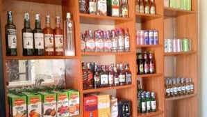 A liquor store with shelves stocked with various bottles of alcohol, canned beverages, and boxes of snacks. - Clinton Hotel (Kikuyu)