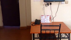 A small room with a wooden table, a black chair, a flat-screen TV mounted on the wall, a telephone, and a menu on the table. - Clinton Hotel (Kikuyu)
