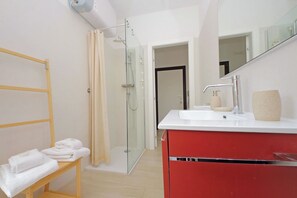 A modern bathroom with a glass shower enclosure, a wooden bench with towels, a red vanity with a mirror, and a white sink. - Rifugio incantato sul fiume Tevere (Rome)