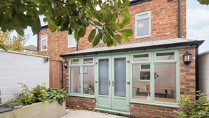A conservatory with a brick exterior and a green door, surrounded by plants and a white wall. - Host & Stay | The Braes (Marske-by-the-Sea)