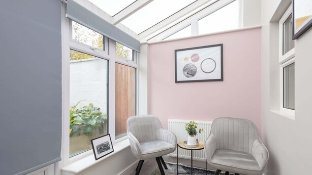 A room with a pink wall, two white chairs, a small table with a plant, and a framed picture. - Host & Stay | The Braes (Marske-by-the-Sea)