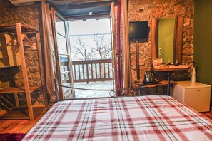 Una habitación con una cama, una estantería de madera, un televisor y una pared de piedra.
