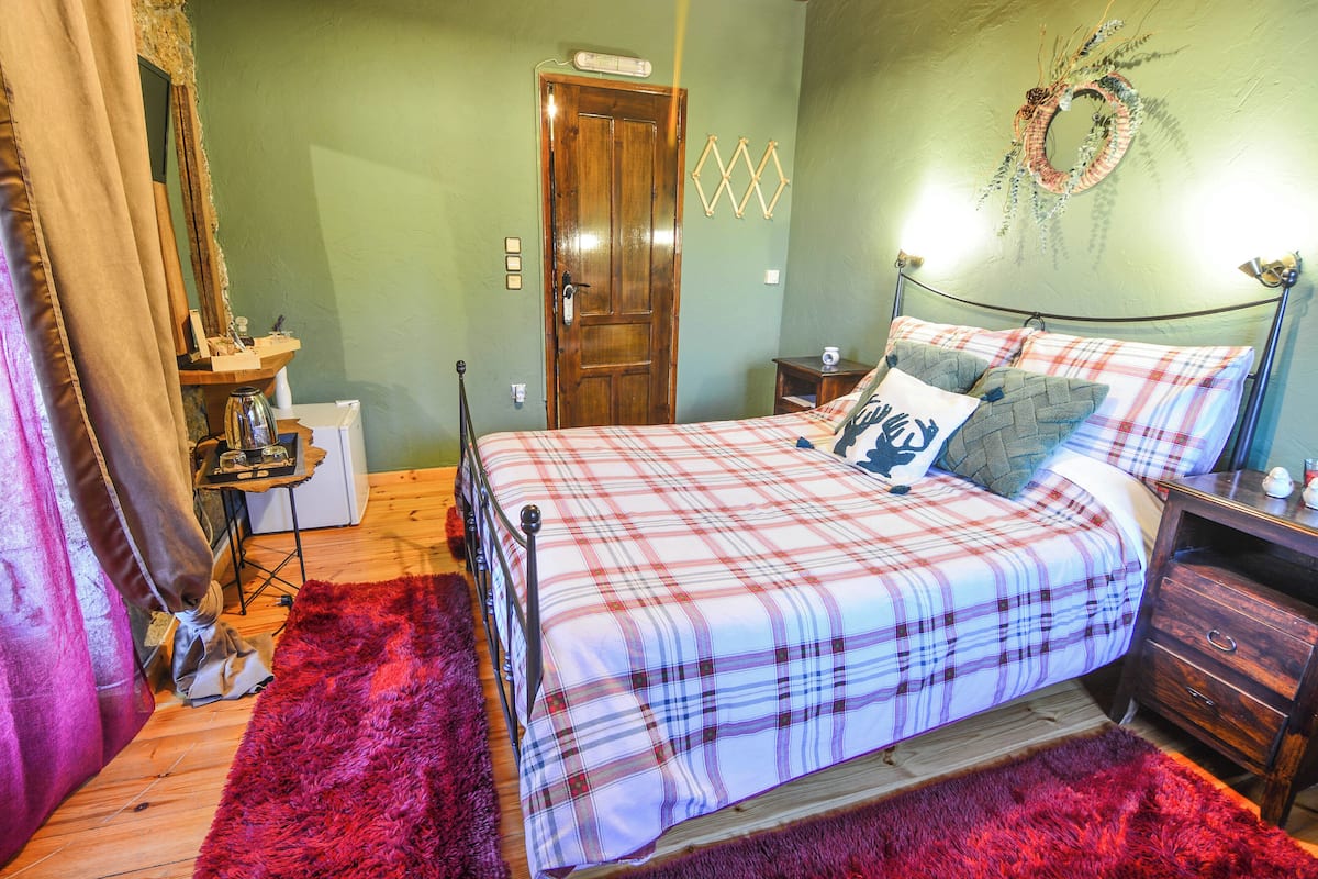 A bedroom with a plaid bedspread, a wooden door, a small bedside table, and a red rug.