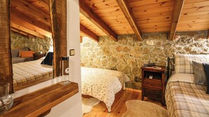 A bedroom with a stone wall, wooden ceiling beams, and two beds with plaid bedding.