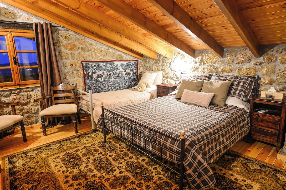 A bedroom with a bed, a chair, a nightstand, and a stone wall.
