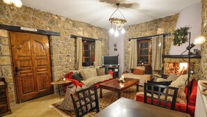 A cozy living room with stone walls, a wooden door, a fireplace, a television, and a dining area with a table and chairs.