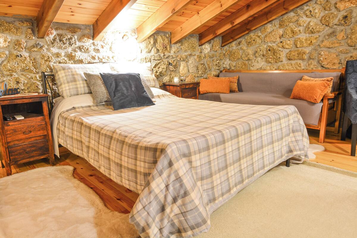 A bedroom with a checkered bedspread, a stone wall, wooden beams, and a cozy atmosphere.