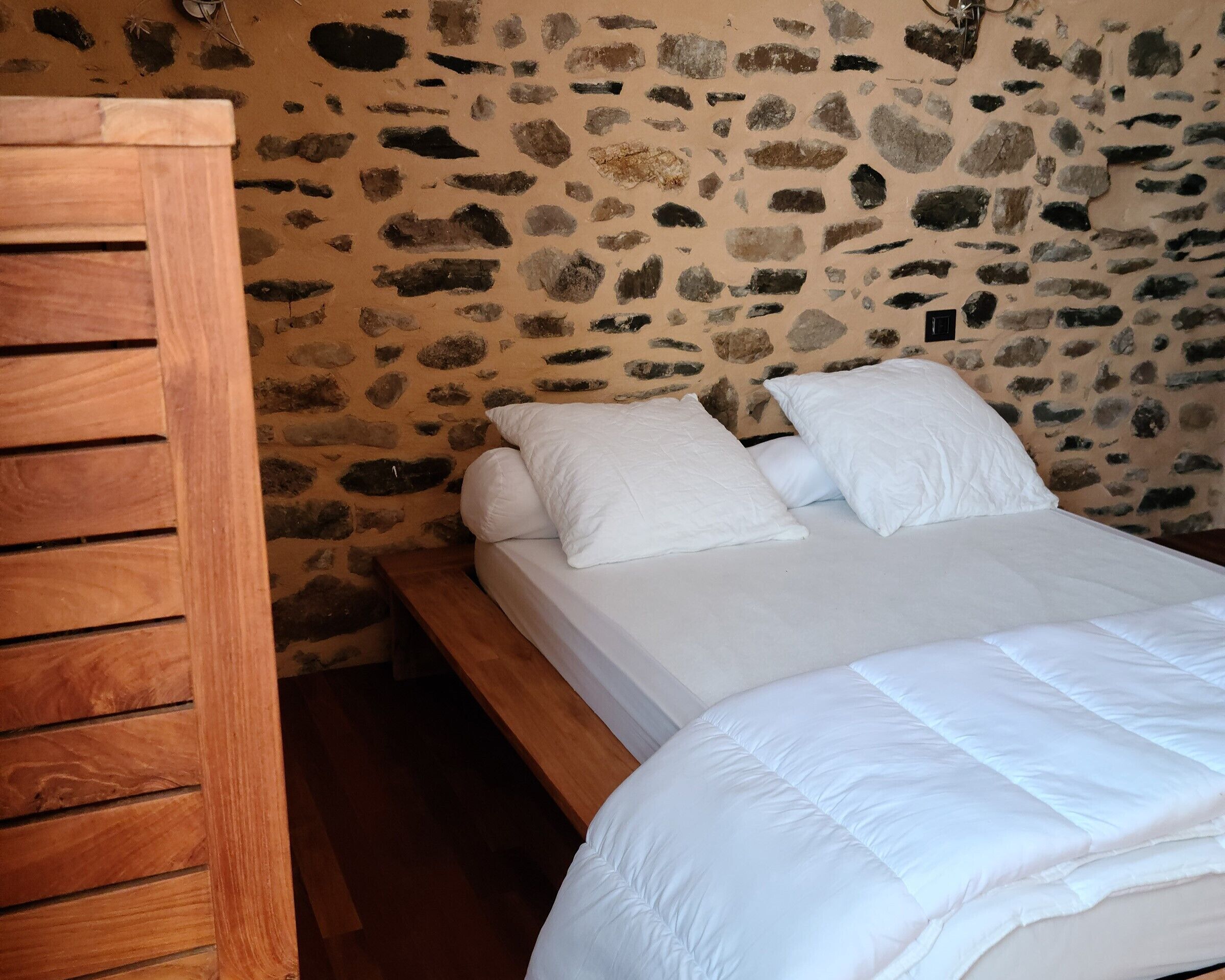 A bed with white bedding in a room with a stone wall.