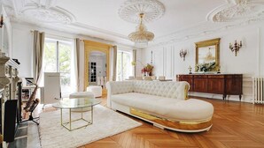 Un salón amplio con un sofá blanco, una mesa de centro de vidrio y una imponente lámpara de araña.