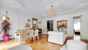 Una habitación amplia con suelo de parqué, muebles blancos y una gran lámpara de araña.