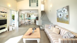 Ein großzügiger Wohnbereich mit einer Couch, einem Couchtisch und einem Fernseher. Eine Treppe führt zu einer oberen Ebene.