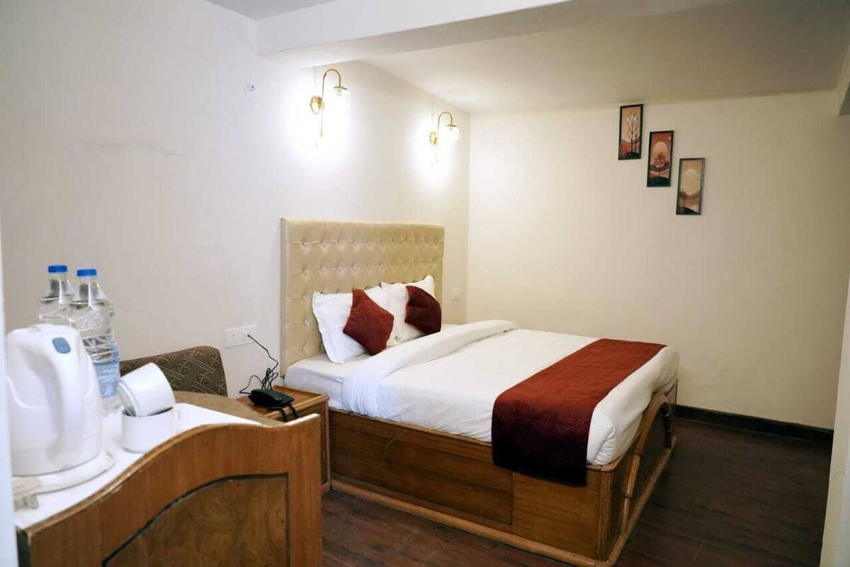 Una habitación de hotel con una cama de madera, una mesita de noche con hervidor y un dispensador de agua.