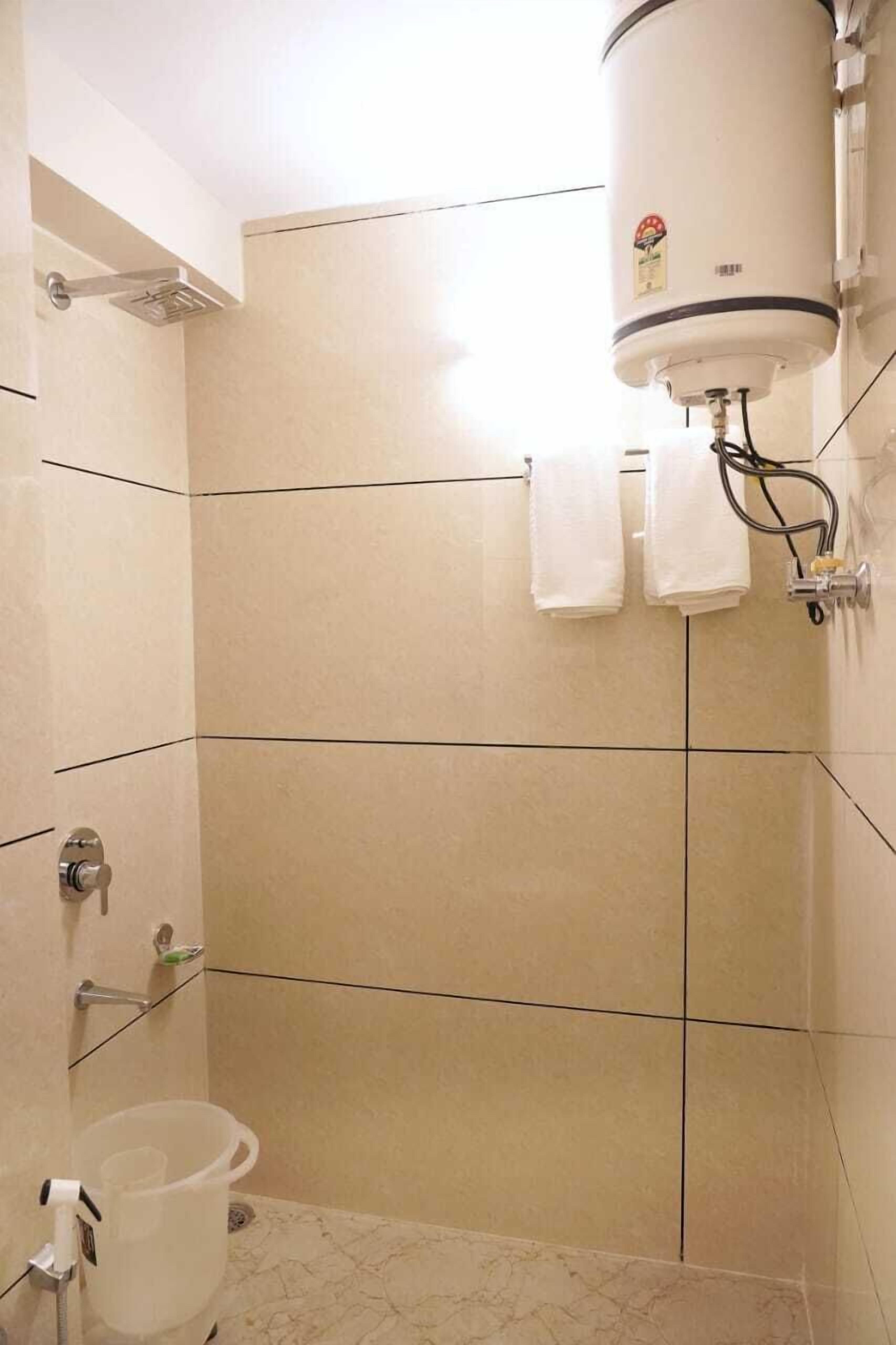 A bathroom with beige tiled walls, a white showerhead, and a white bucket.