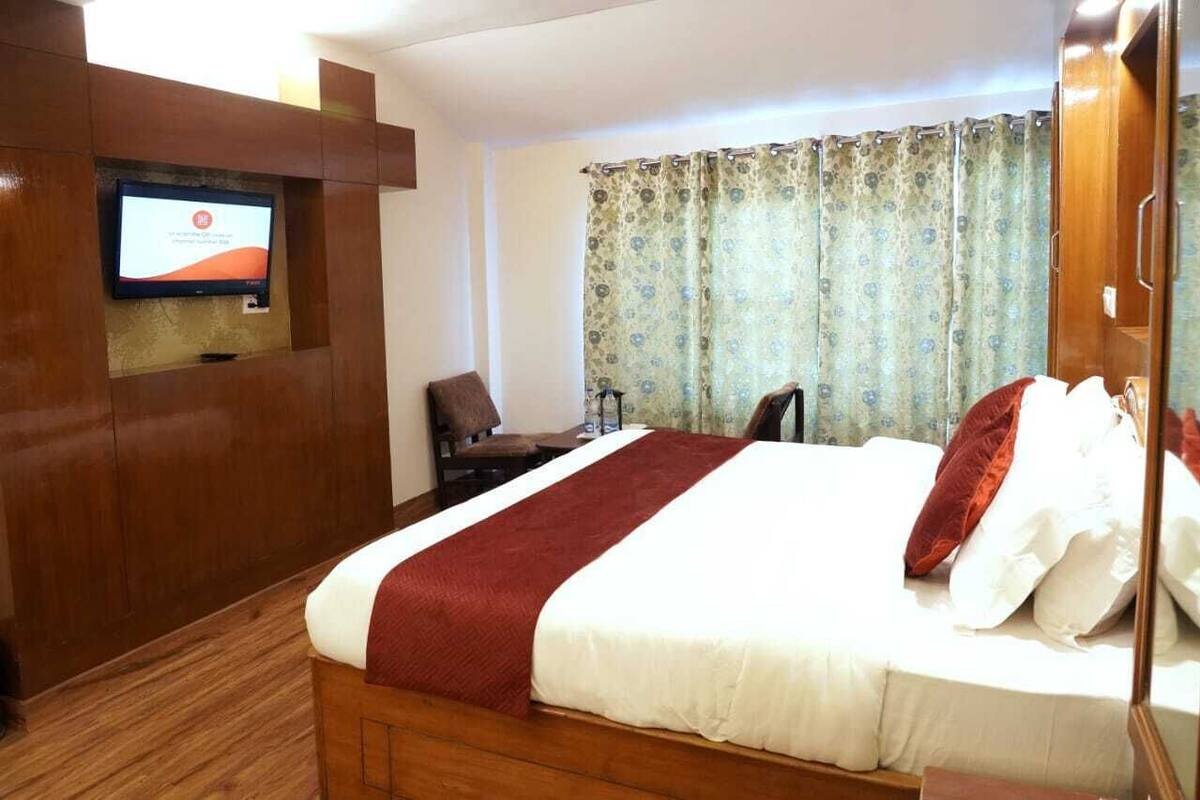 Habitación de hotel con una cama grande, un televisor montado en un panel de madera, un escritorio con una silla y una cortina con estampado floral.