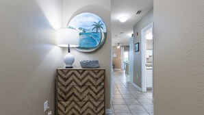 A hallway with a chevron-patterned cabinet, a round painting of a beach scene, and a lamp. - Charming 1BR/1B~sleeps 6~Gym, Pool, & Boat Parking (Orange Beach)