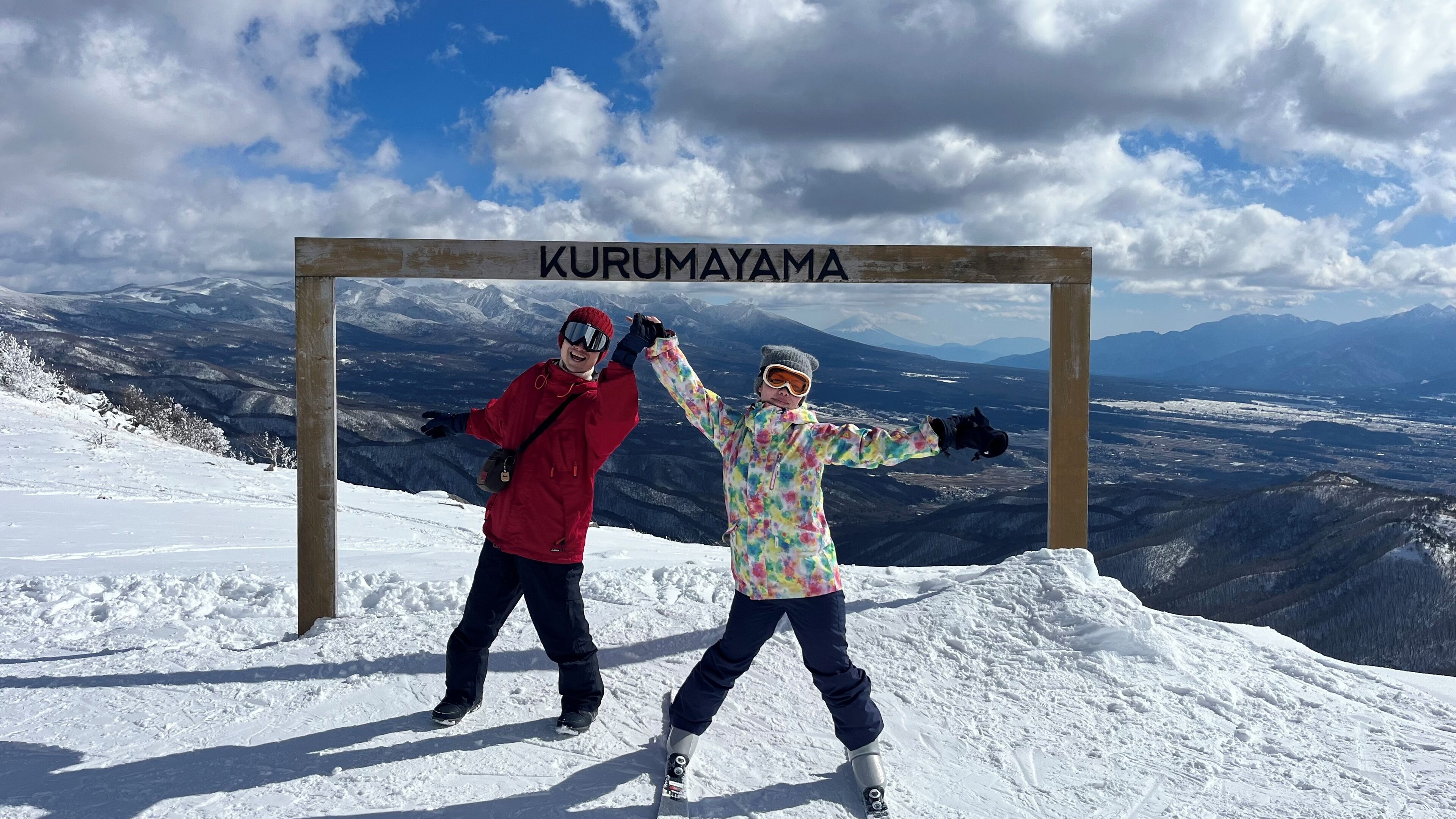 A wooden sign with 'KURUMAYAMA' written on it, set against a snowy mountain landscape with a clear sky.