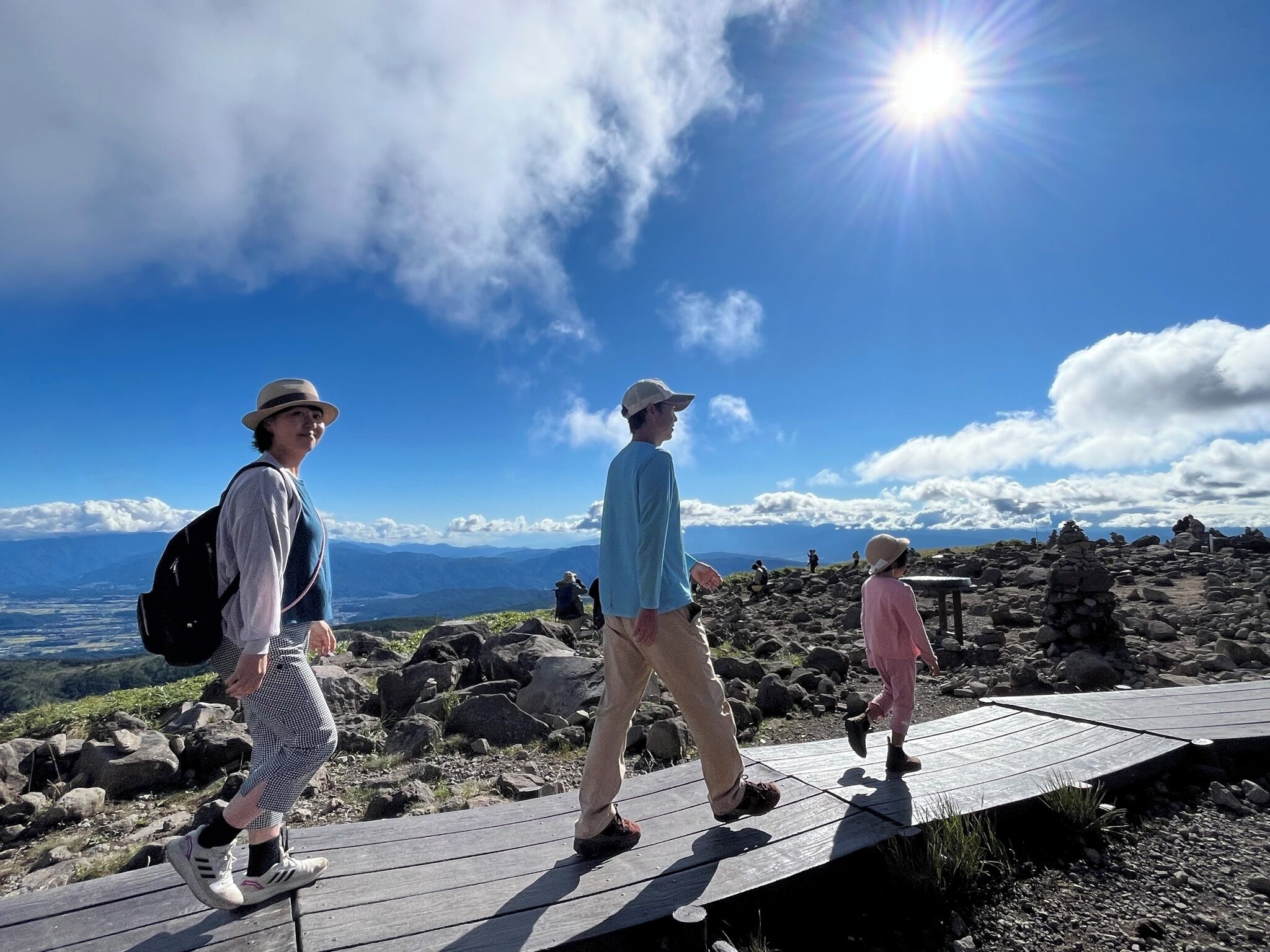 A wooden pathway with a clear view of distant mountains and a bright sun in the sky.
