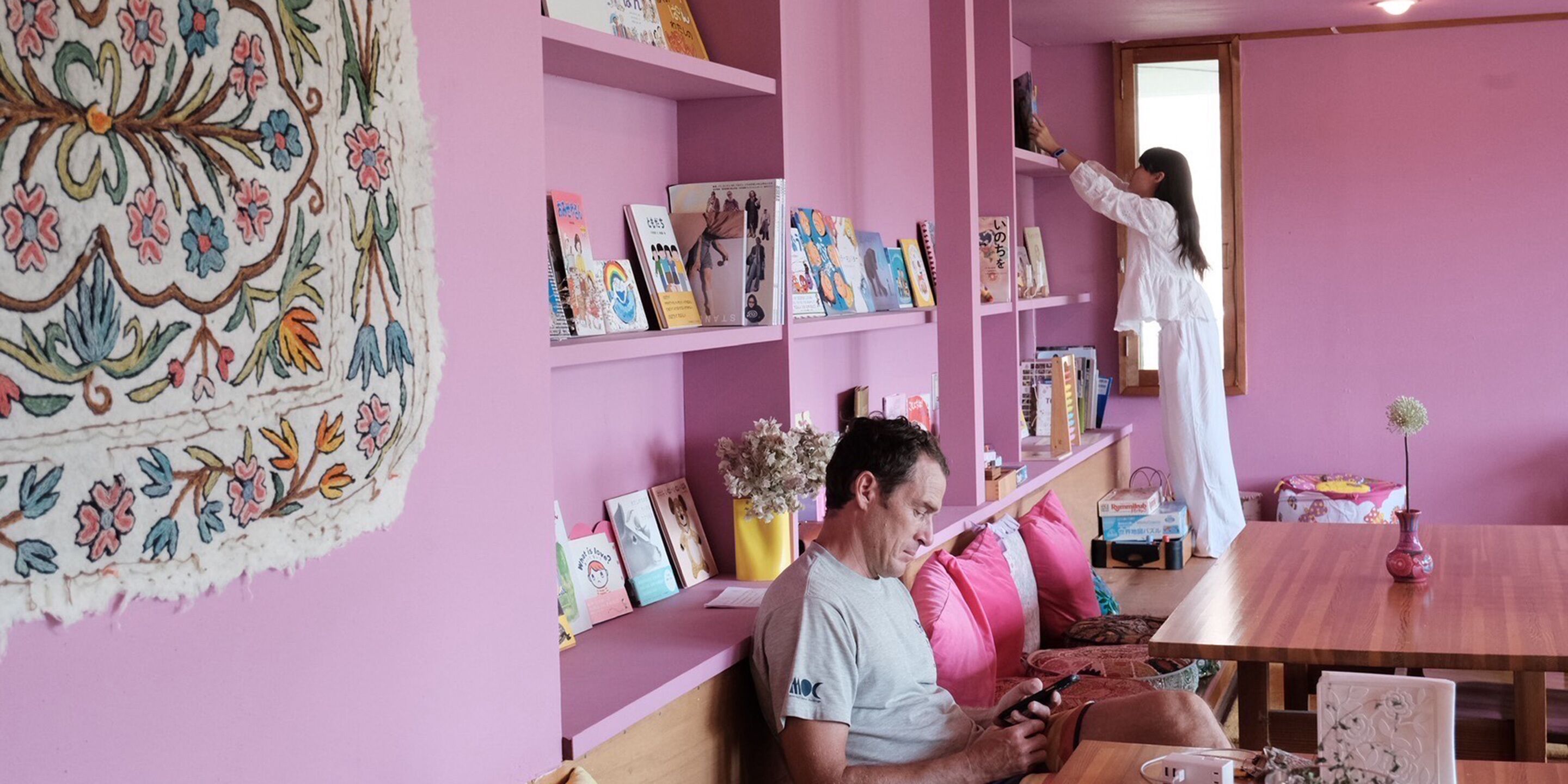 Una habitación con paredes rosas, una mesa de madera y estantes con libros y adornos.
