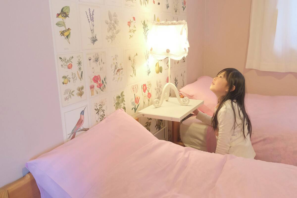 Et værelse med en seng, et natbord med en lampe og en væg pyntet med botaniske illustrationer.