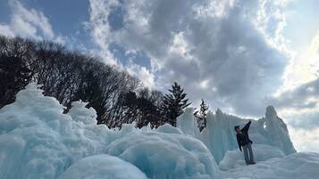 Eine Person steht auf einer schneeüberzogenen Eisskulptur, im Hintergrund sind Bäume zu sehen.