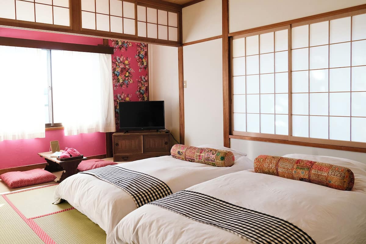 Et traditionelt japansk værelse med tatamimåtter, en futonmadras, et fjernsyn på et træskab og en skydedør af shoji-papir.