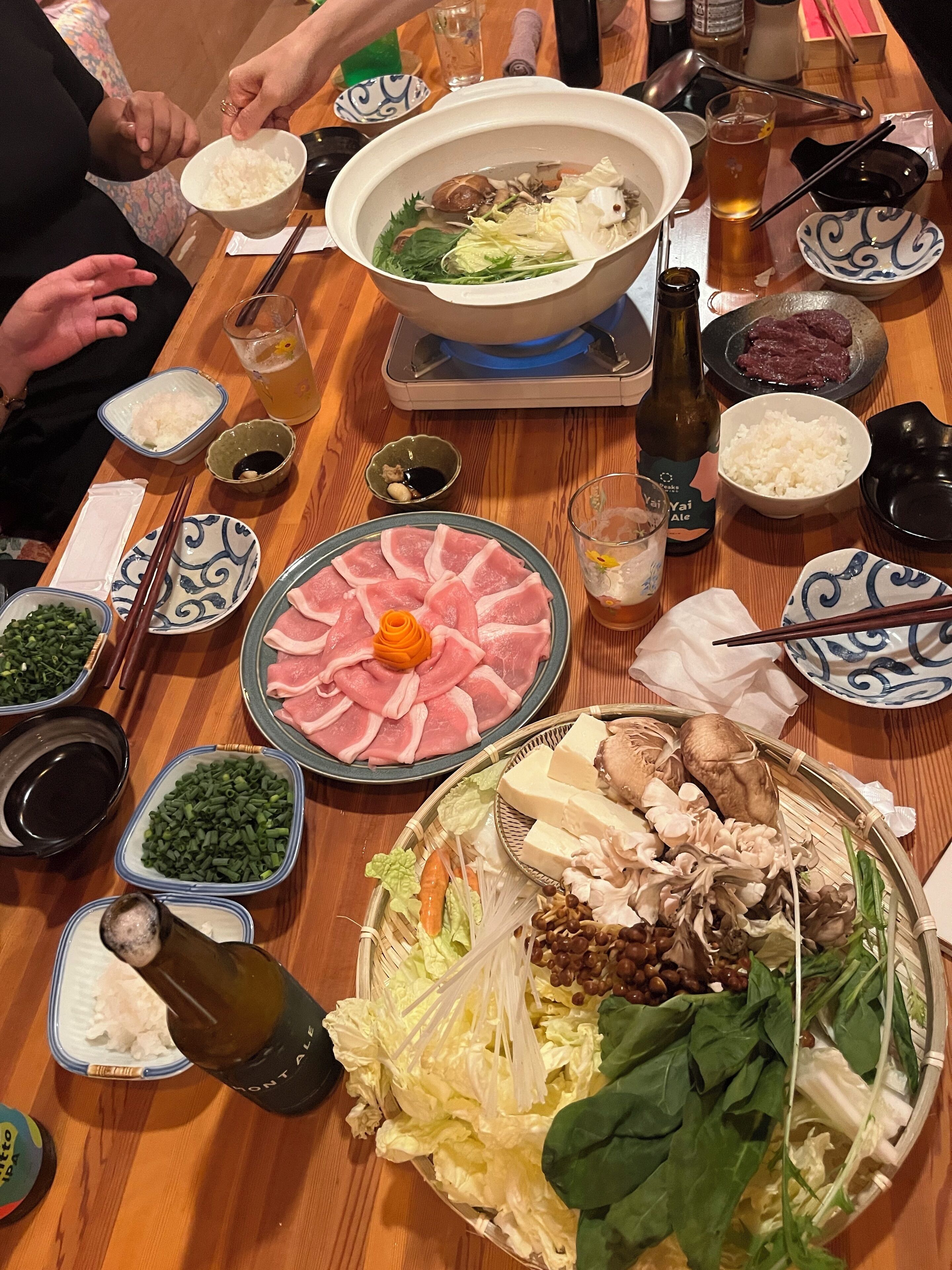 A dining table with various food items, including a hot pot, plates of sliced meat, and bowls of vegetables.