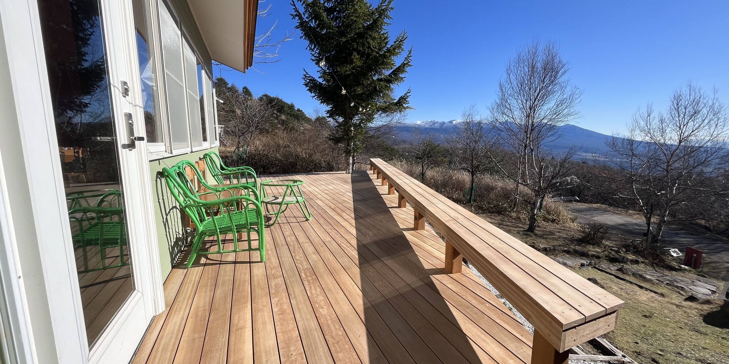 Eine Holzterrasse mit grünen Stühlen und Bänken, mit Blick auf eine gebirgige Landschaft.