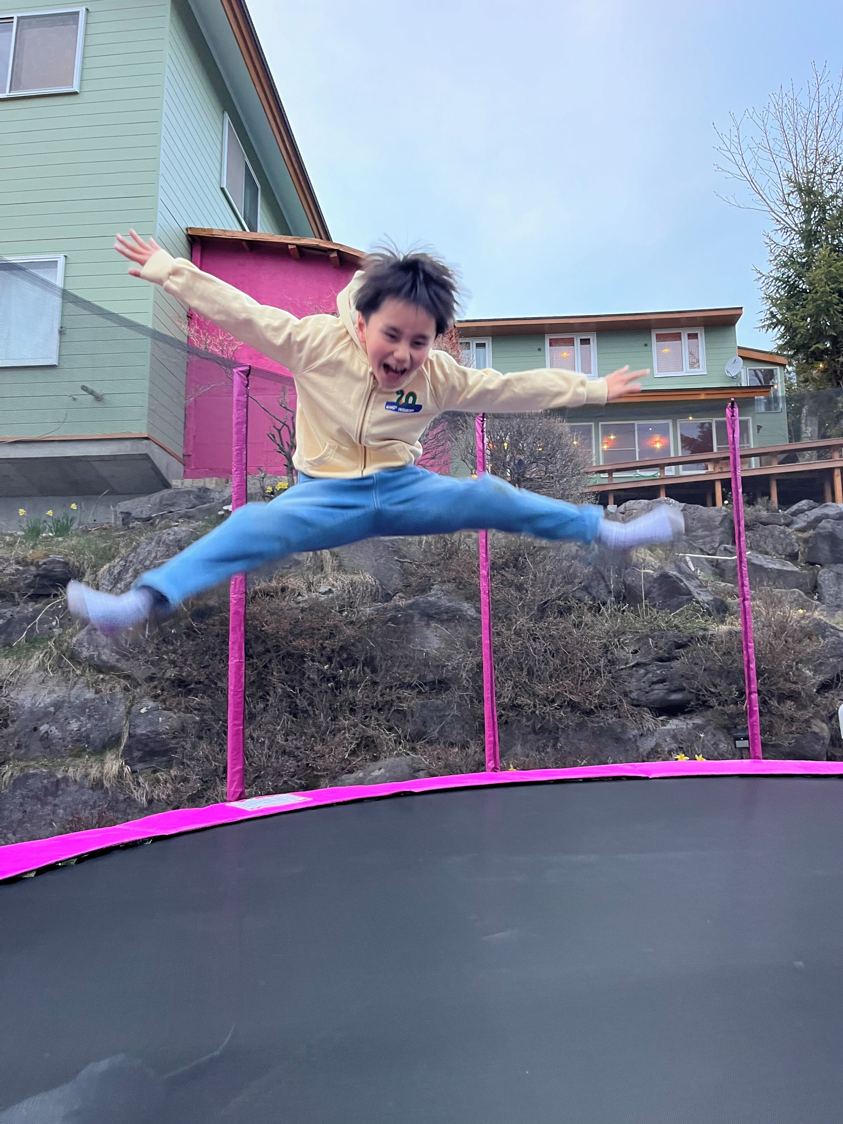 A child jumping on a trampoline in front of a house.