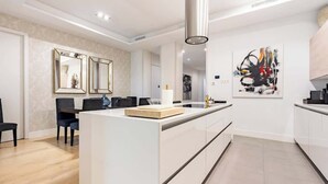 Una cocina moderna con una isla central, armarios blancos y un comedor con sillas y una mesa.