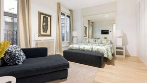 Una habitación de hotel moderna con una cama grande, un sofá negro, una mesita y un espejo amplio.