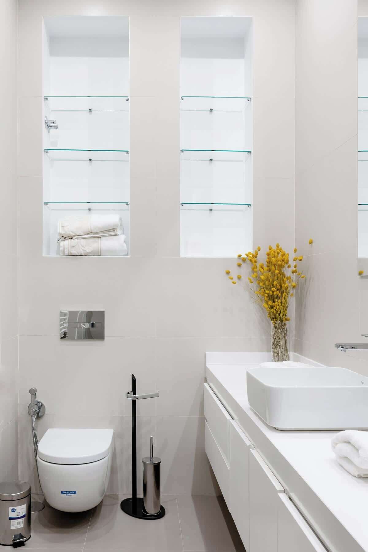 A modern bathroom with a toilet, bidet, and a sink with a glass shelf above.