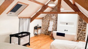 A bedroom with a sloped ceiling, wooden beams, a stone wall, a bathtub, and a bed with a headboard. - La Maison Gavraise - Stunning house (and Attached Barn) in the Centre of Gavray. (Gavray-sur-Sienne)