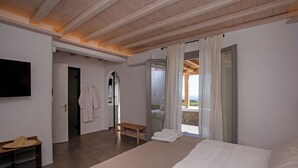 Een moderne slaapkamer met een groot bed, een houten bankje, een aan de muur bevestigde televisie en uitzicht op de omgeving via een glazen deur.