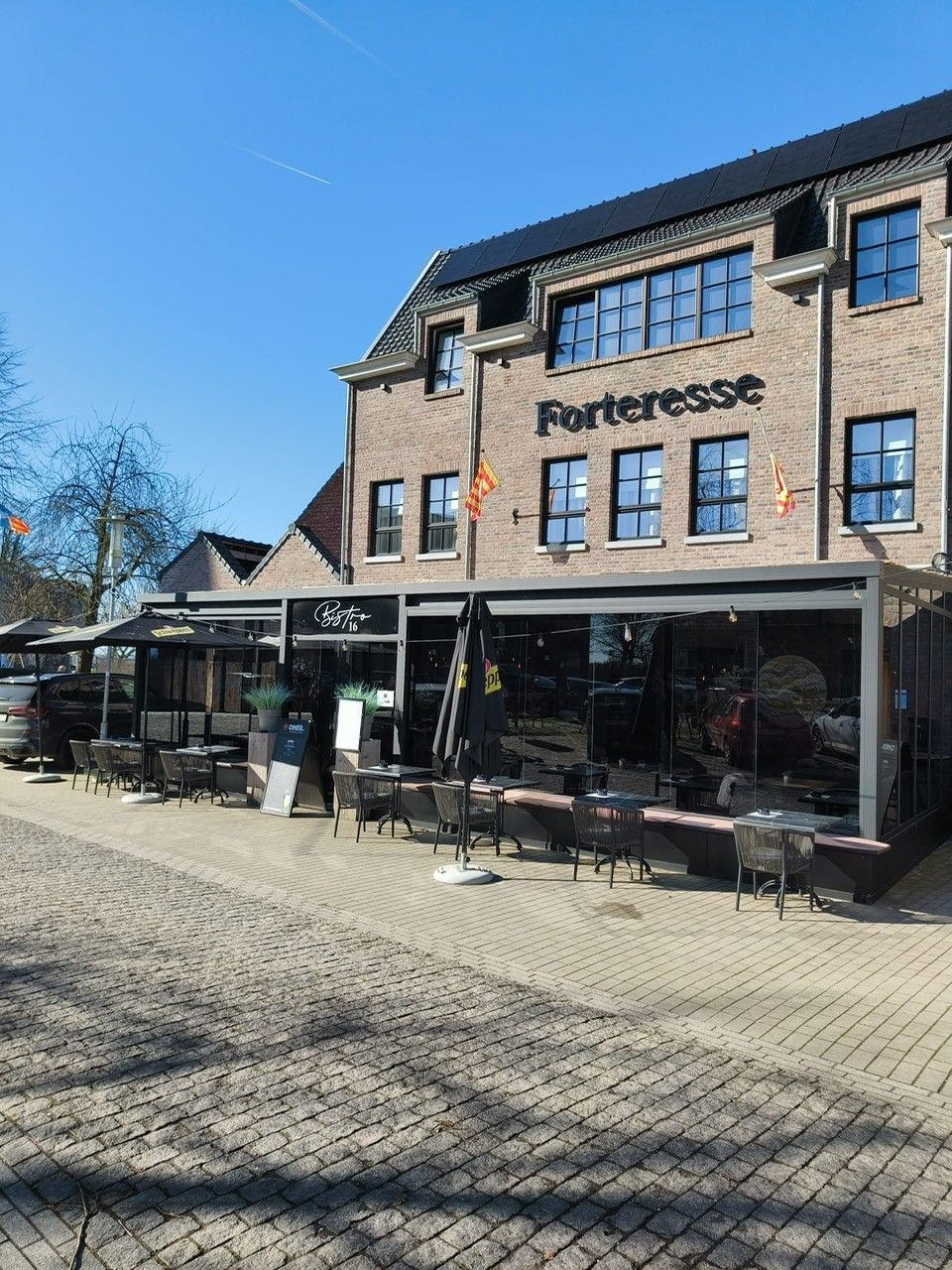 Een gebouw van baksteen met een winkelgevel, genaamd 'Forteresse', en een terras.