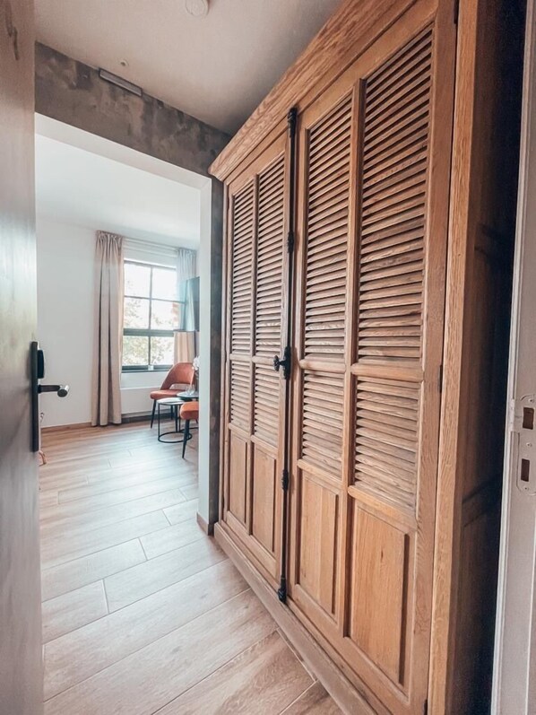 A hallway with a wooden wardrobe, a chair, and a window with curtains. - La Forteresse (Borgloon)
