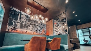 Interno di un ristorante con un murale vintage in bianco e nero, sedute color petrolio e illuminazione a sospensione.