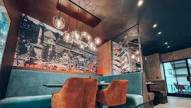 A restaurant interior with a vintage black and white photo mural, teal seating, and pendant lighting.