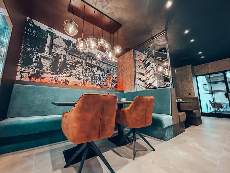 Interior de un restaurante con un mural fotográfico en blanco y negro de estilo vintage, asientos color turquesa e iluminación colgante.