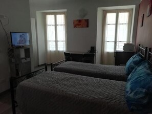 A hotel room with two beds, a desk, and a television. - L'Angelo (Omegna)