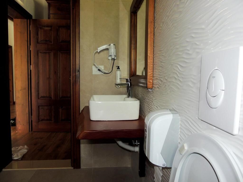 A bathroom with a wooden door, a white sink, a mirror, and a white toilet.