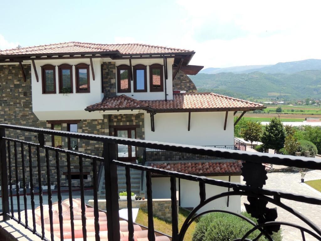 A two-story house with a stone facade, a tiled roof, and a balcony with a wrought iron railing.