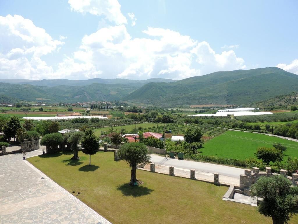 A landscaped area with a paved walkway, trees, and a view of distant hills.