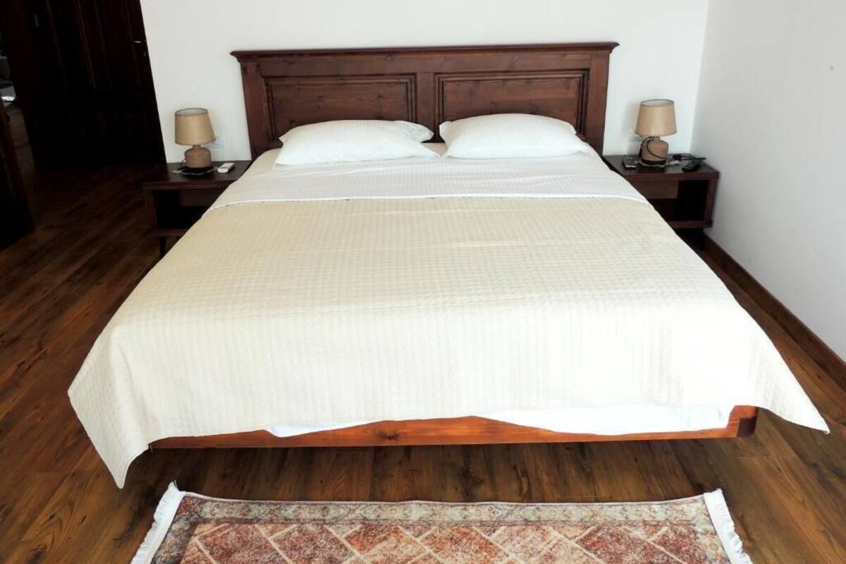 A large bed with a wooden headboard, two bedside tables with lamps, and a patterned rug on the floor.