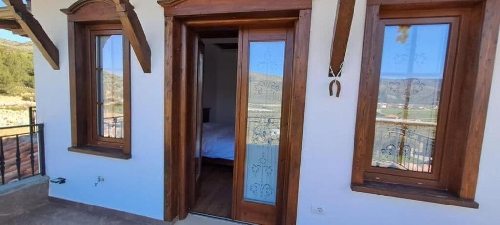 A room with a wooden door, a balcony, and a view of the landscape.