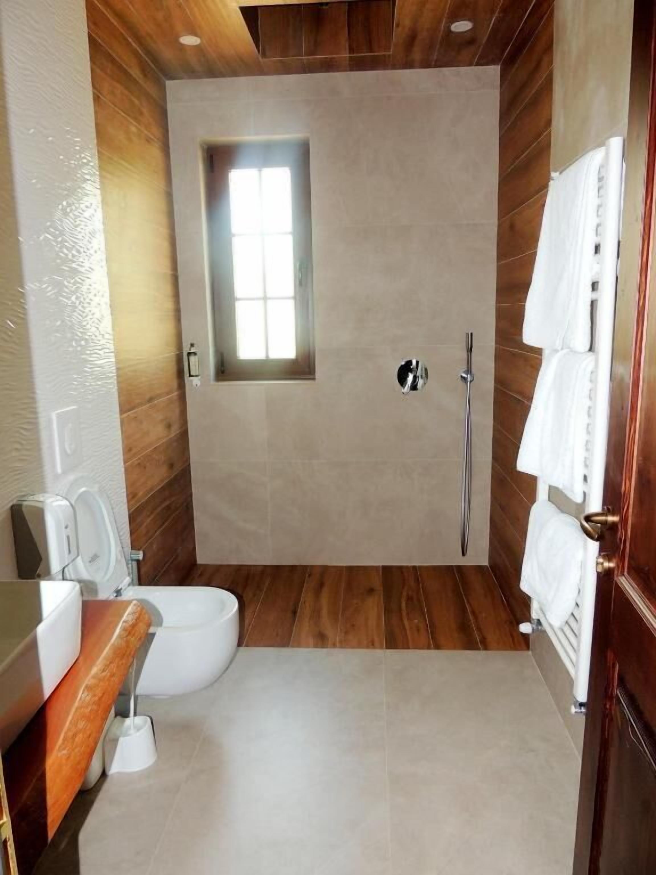 Een moderne badkamer met een houten vloer, een inbouw raam, een douche en een toilet.
